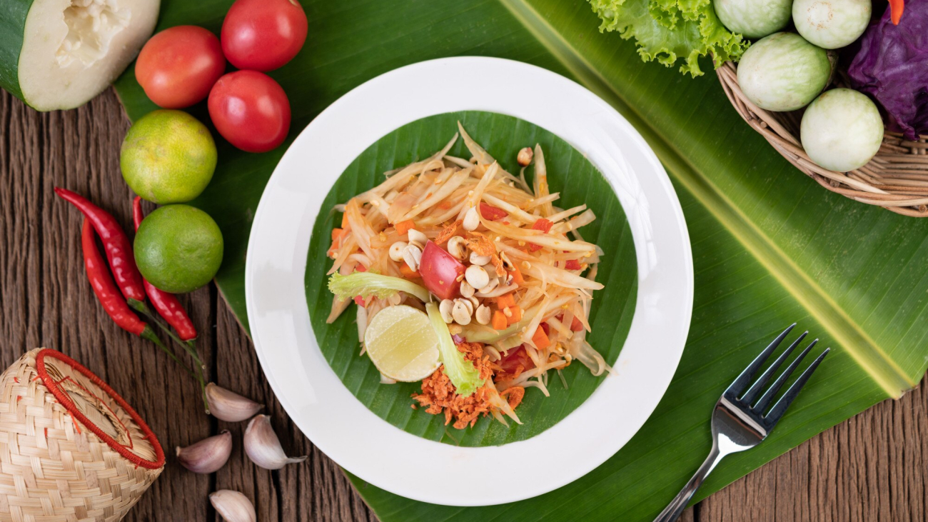 thai-papaya-salad-white-plate-banana-leaves-with-lime-tomatoes-eggplant-chili-garlic-peppers-salad-peanuts_1150-20731